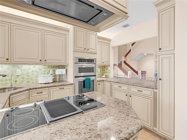 kitchen featuring decorative backsplash, cream cabinetry, double oven, and light stone countertops