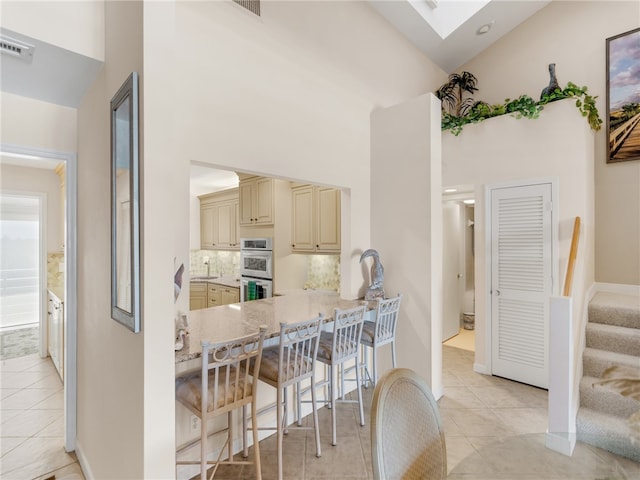 kitchen featuring light tile patterned flooring, a towering ceiling, a kitchen breakfast bar, double oven, and cream cabinetry