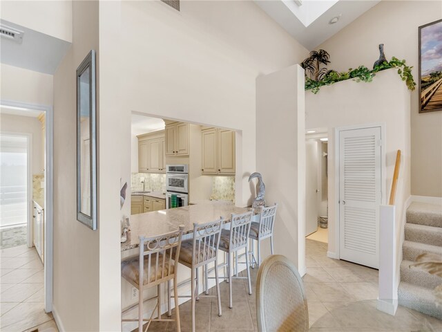 8444 Oceanside Dr Unit D31, Indian River Shores, FL 32963 - kitchen with cream cabinetry, a high ceiling, stainless steel double oven, light tile patterned floors, and a breakfast bar