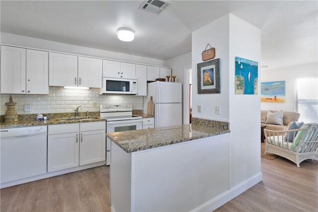 kitchen with white appliances, dark stone counters, white cabinets, sink, and light wood-type flooring