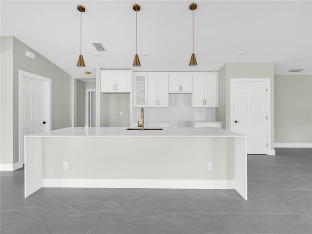 kitchen featuring sink, an island with sink, vaulted ceiling, decorative light fixtures, and white cabinets