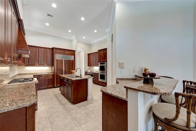 kitchen with sink, appliances with stainless steel finishes, light stone counters, a kitchen island with sink, and crown molding