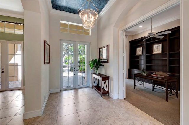 carpeted foyer with french doors, ceiling fan with notable chandelier, and crown molding