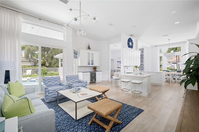 living room featuring light hardwood / wood-style flooring, sink, beverage cooler, and an inviting chandelier