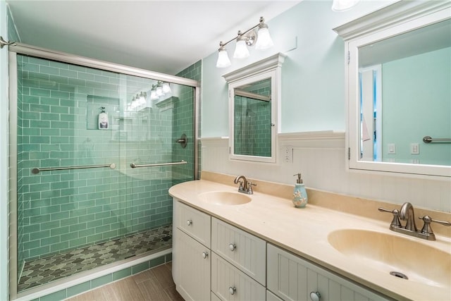 full bath featuring a wainscoted wall, a sink, a shower stall, and double vanity