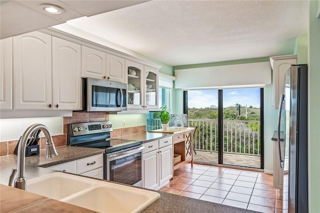 kitchen with stainless steel appliances, dark countertops, glass insert cabinets, white cabinetry, and a sink