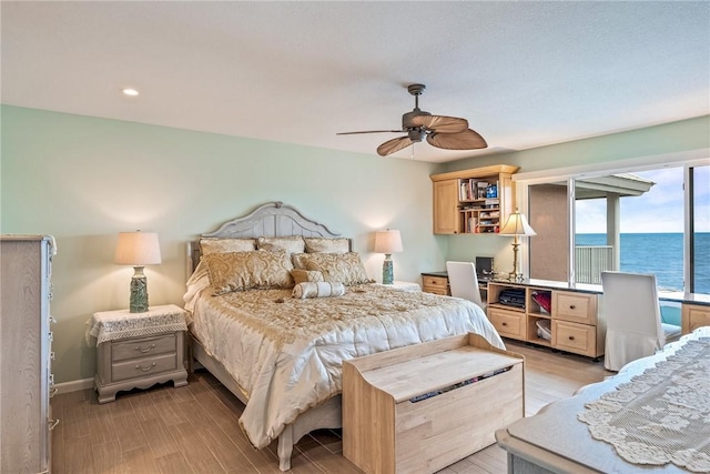 bedroom with a water view, light wood finished floors, baseboards, and a ceiling fan