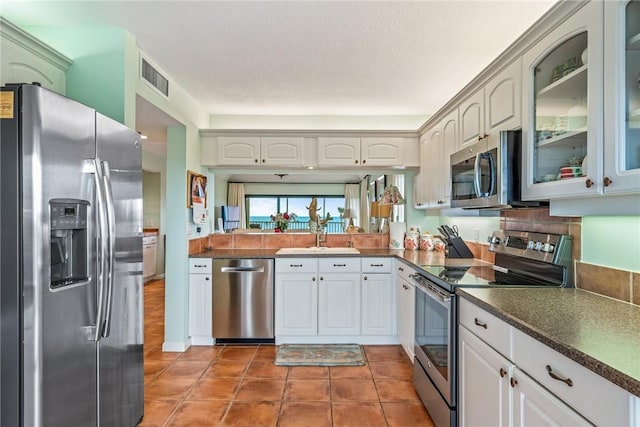 kitchen featuring dark countertops, visible vents, appliances with stainless steel finishes, glass insert cabinets, and a sink