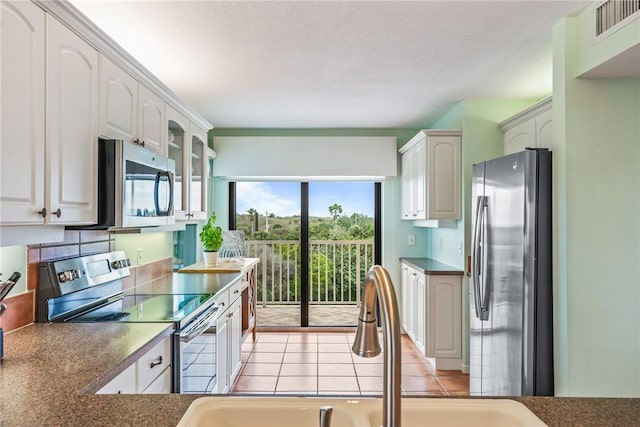 kitchen with light tile patterned floors, stainless steel appliances, a sink, white cabinets, and glass insert cabinets