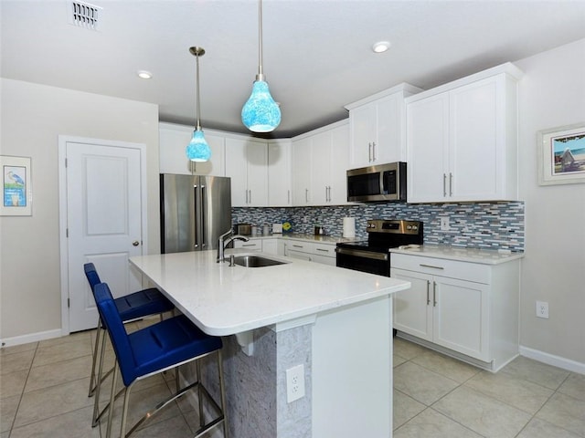 kitchen featuring stainless steel appliances, sink, white cabinetry, hanging light fixtures, and a kitchen island with sink