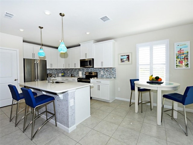 kitchen featuring appliances with stainless steel finishes, white cabinetry, decorative light fixtures, and an island with sink