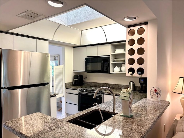 kitchen with kitchen peninsula, dark stone counters, sink, white cabinetry, and stainless steel refrigerator