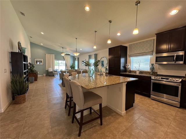 kitchen with stainless steel appliances, pendant lighting, vaulted ceiling, a breakfast bar, and a kitchen island with sink