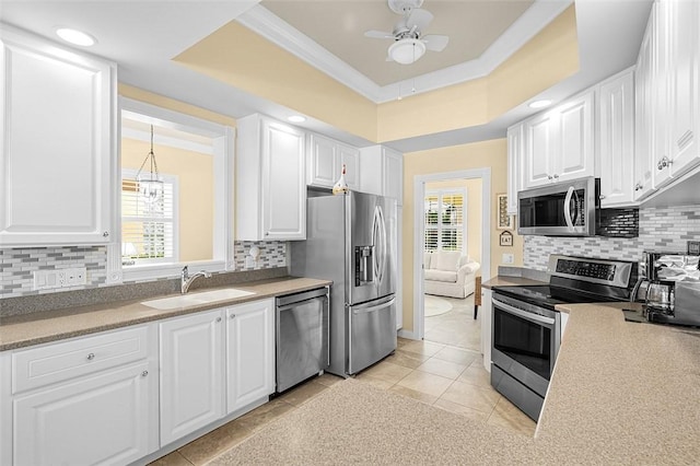 kitchen with stainless steel appliances, a sink, a healthy amount of sunlight, white cabinets, and a tray ceiling