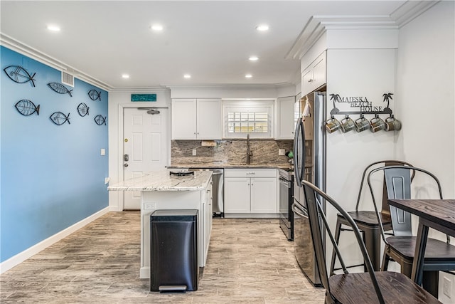 kitchen with white cabinetry, light stone countertops, a center island, light hardwood / wood-style flooring, and crown molding