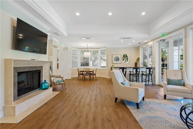 living area featuring wood finished floors, visible vents, a tray ceiling, a high end fireplace, and ornamental molding