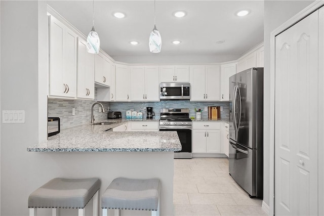 kitchen with kitchen peninsula, a kitchen bar, stainless steel appliances, white cabinetry, and hanging light fixtures