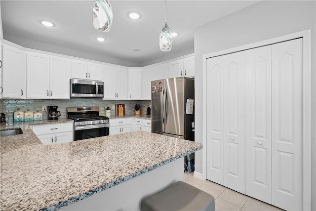 kitchen with pendant lighting, kitchen peninsula, appliances with stainless steel finishes, light tile patterned flooring, and white cabinetry