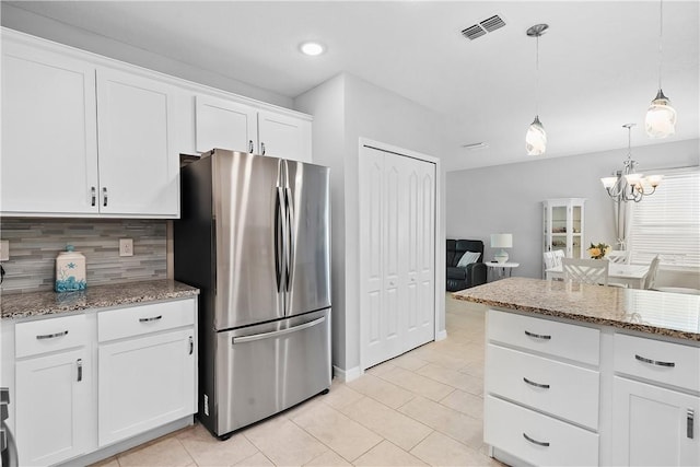 kitchen featuring stainless steel refrigerator, white cabinetry, light stone counters, backsplash, and decorative light fixtures