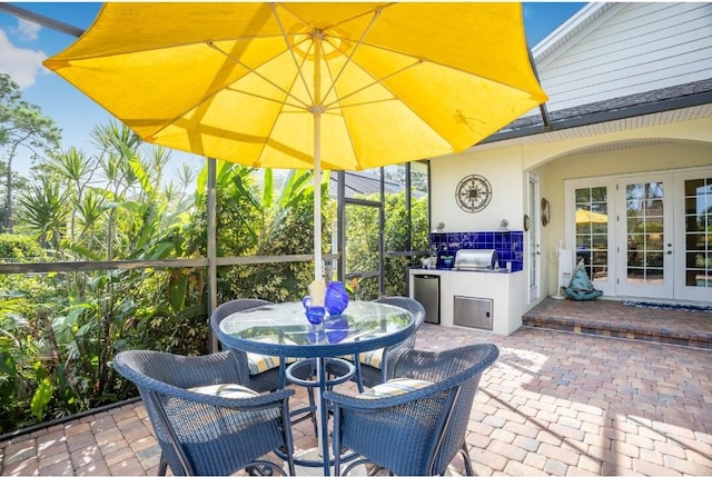 view of patio featuring glass enclosure, french doors, and grilling area