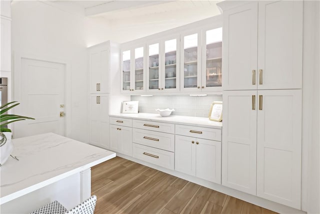 kitchen with white cabinets, lofted ceiling with beams, light stone countertops, and backsplash