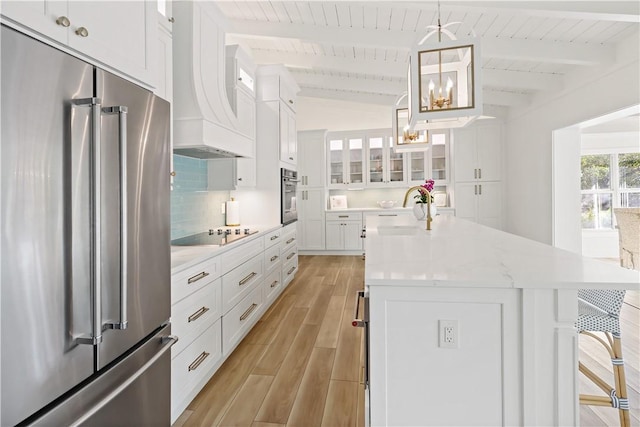 kitchen featuring appliances with stainless steel finishes, an island with sink, white cabinets, decorative light fixtures, and backsplash