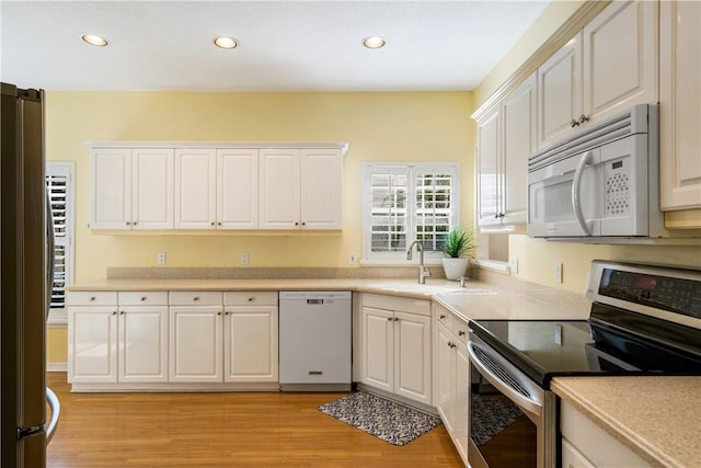 kitchen with sink, white appliances, light hardwood / wood-style flooring, and white cabinets