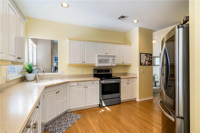 kitchen with stainless steel appliances, white cabinetry, sink, and light hardwood / wood-style floors