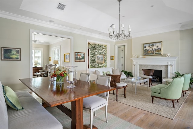 dining space featuring visible vents, light wood-style flooring, an inviting chandelier, crown molding, and a fireplace