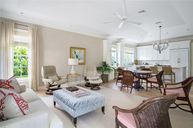 living room with a raised ceiling, visible vents, light wood-style flooring, baseboards, and ceiling fan with notable chandelier