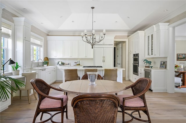 dining space with light wood-style floors, a raised ceiling, a notable chandelier, and ornamental molding