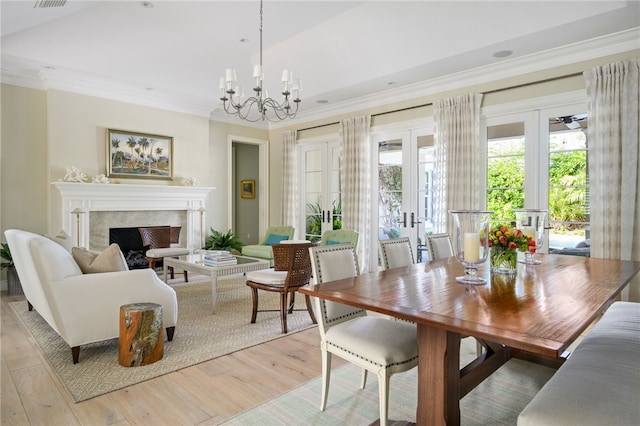 interior space with a fireplace, light wood-style floors, french doors, an inviting chandelier, and crown molding