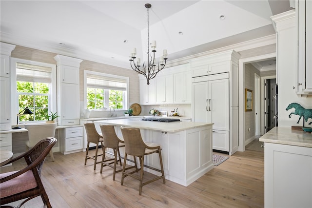 kitchen featuring light wood-style flooring, a center island, crown molding, paneled fridge, and white cabinetry