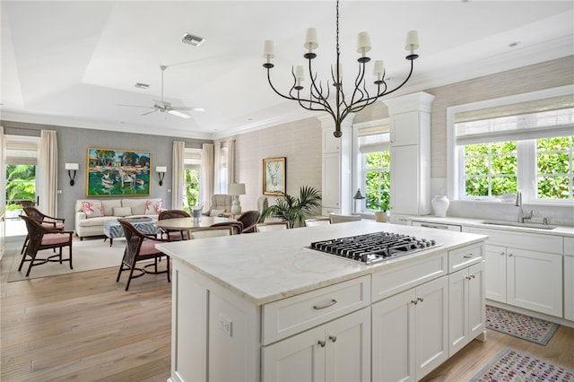 kitchen with ornamental molding, a center island, light wood-style floors, stainless steel gas cooktop, and a sink