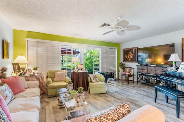 living room with ceiling fan, a textured ceiling, and light wood-type flooring