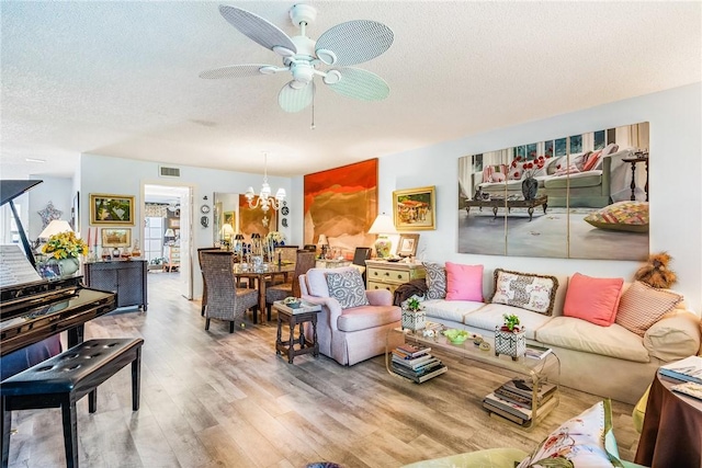 living room with ceiling fan with notable chandelier, hardwood / wood-style floors, and a textured ceiling