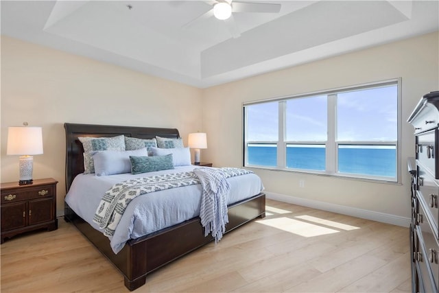 bedroom featuring a water view, ceiling fan, a tray ceiling, and light hardwood / wood-style floors