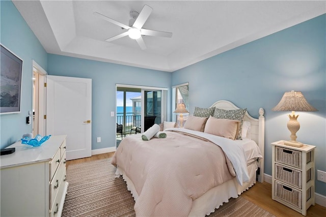 bedroom featuring ceiling fan, access to exterior, light hardwood / wood-style floors, and a tray ceiling