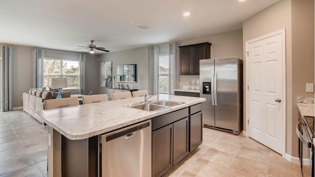 kitchen with dark brown cabinetry, stainless steel appliances, ceiling fan, a kitchen island with sink, and sink