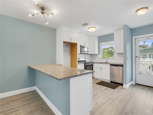 kitchen with kitchen peninsula, appliances with stainless steel finishes, tasteful backsplash, light hardwood / wood-style floors, and white cabinetry