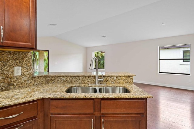 kitchen with kitchen peninsula, light stone counters, sink, hardwood / wood-style floors, and lofted ceiling