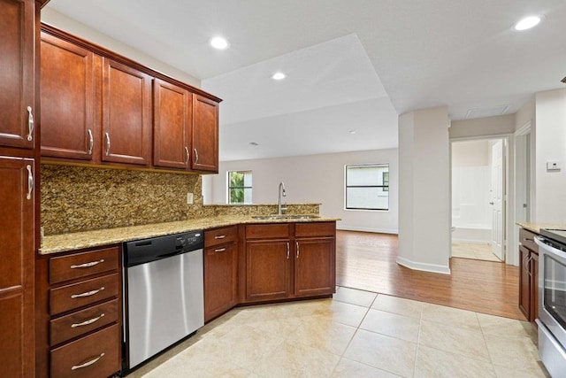 kitchen with kitchen peninsula, light stone counters, stainless steel appliances, sink, and light hardwood / wood-style flooring