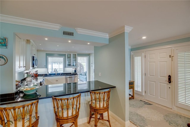 kitchen featuring stainless steel appliances, white cabinetry, a kitchen breakfast bar, kitchen peninsula, and crown molding