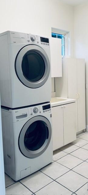 clothes washing area with light tile patterned floors, stacked washer / dryer, and cabinet space