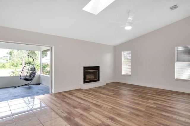 unfurnished living room featuring a tiled fireplace, a wealth of natural light, lofted ceiling with skylight, and light hardwood / wood-style flooring