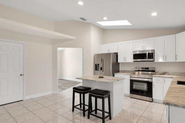 kitchen featuring lofted ceiling with skylight, a kitchen island, white cabinetry, a breakfast bar area, and stainless steel appliances