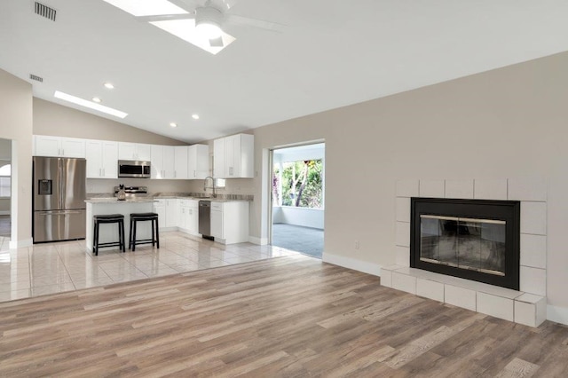 unfurnished living room featuring lofted ceiling, sink, light hardwood / wood-style flooring, ceiling fan, and a fireplace