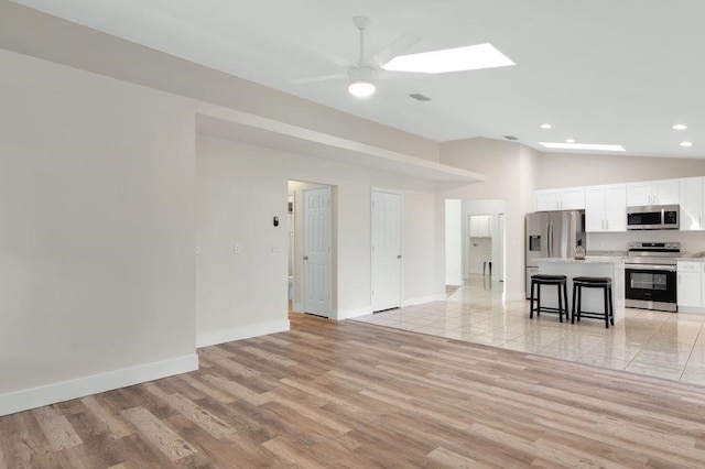 unfurnished living room featuring ceiling fan, vaulted ceiling with skylight, and light hardwood / wood-style floors