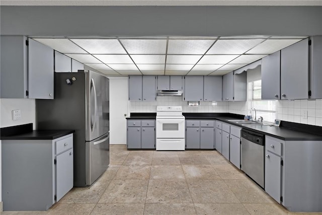 kitchen with a sink, under cabinet range hood, backsplash, dark countertops, and appliances with stainless steel finishes