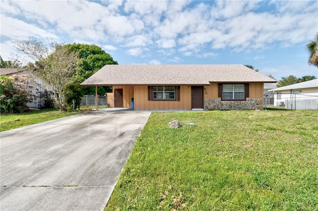 single story home with board and batten siding, a front lawn, fence, concrete driveway, and stone siding